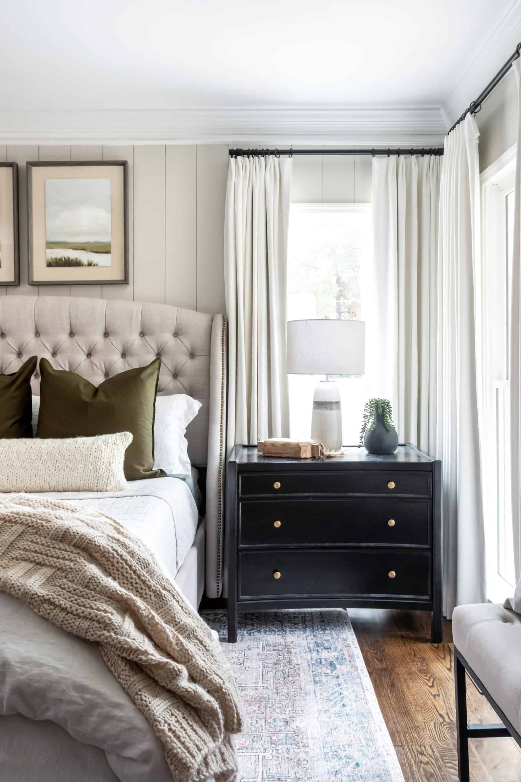 Ivory pinch-pleat curtains on black rods, hung high near the ceiling across a corner window in a cozy bedroom with shiplap walls.